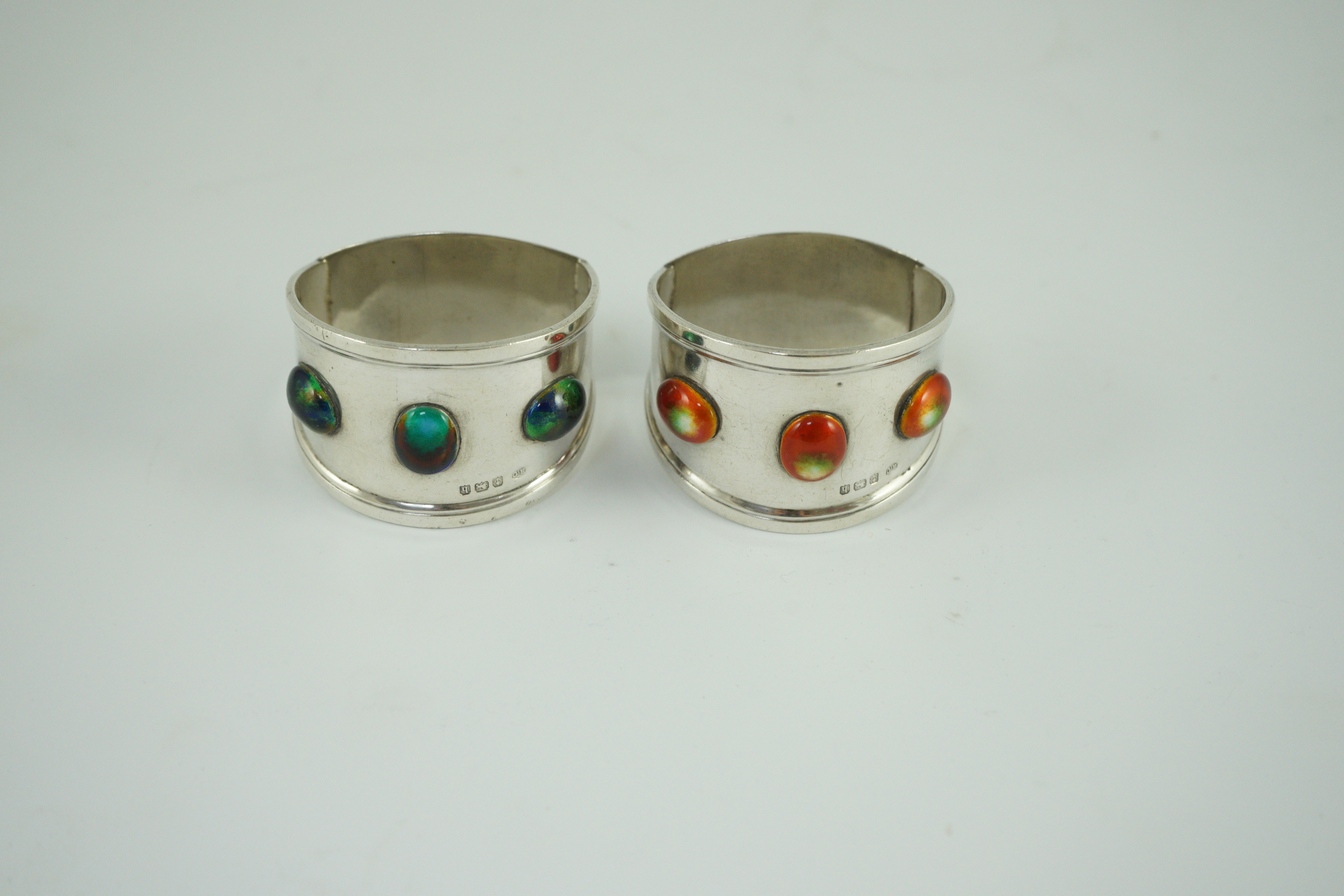 Two similar Edwardian Arts & Crafts silver and enamelled napkin rings